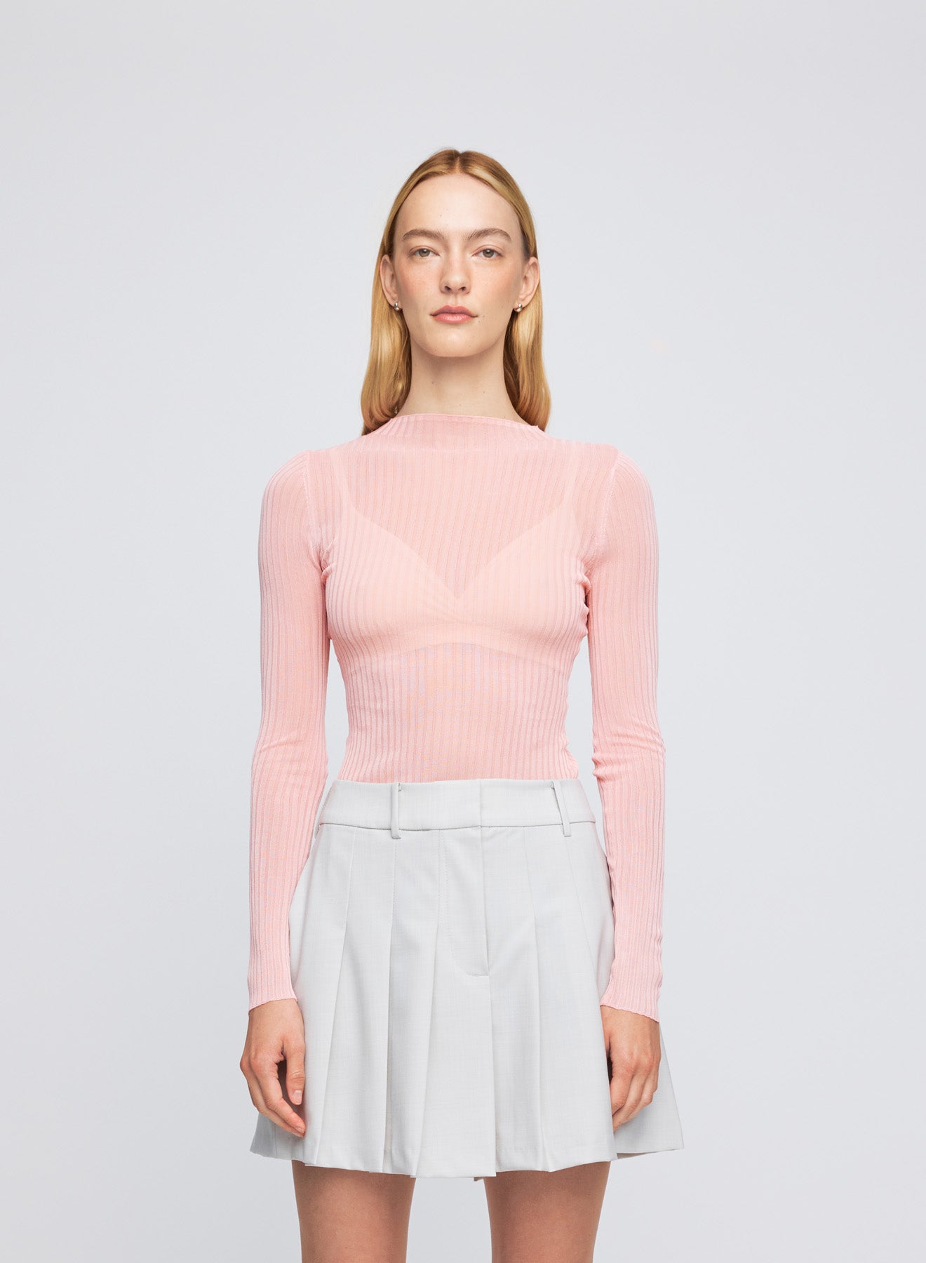 The ANNA QUAN Tatum Top in Sakura is crafted in a sheer knit material with a high boat neckline and long sleeves.